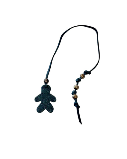 The Henry Beguelin Little Men Bag Charms feature a black string with a small textured teddy bear-shaped charm, gold and black beads, and a handmade logo accent, highlighting the charm of Italian leather craftsmanship.