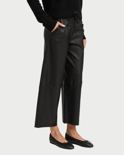 Wearing SPRWMN Cropped Leather Baggy Pants with a drawstring waist, a black sweater, and black ballet flats, a person stands with hands in pockets against a plain background.