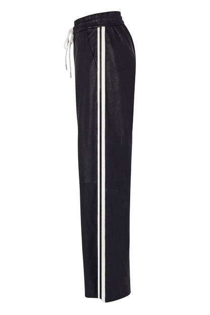 The SPRWMN Baggy Athletic Pants feature black wide-leg styling, an elastic waistband with white drawstring, vertical white side stripes, and side pockets. A relaxed fit adds a modern twist inspired by classic black leather baggy pants.
