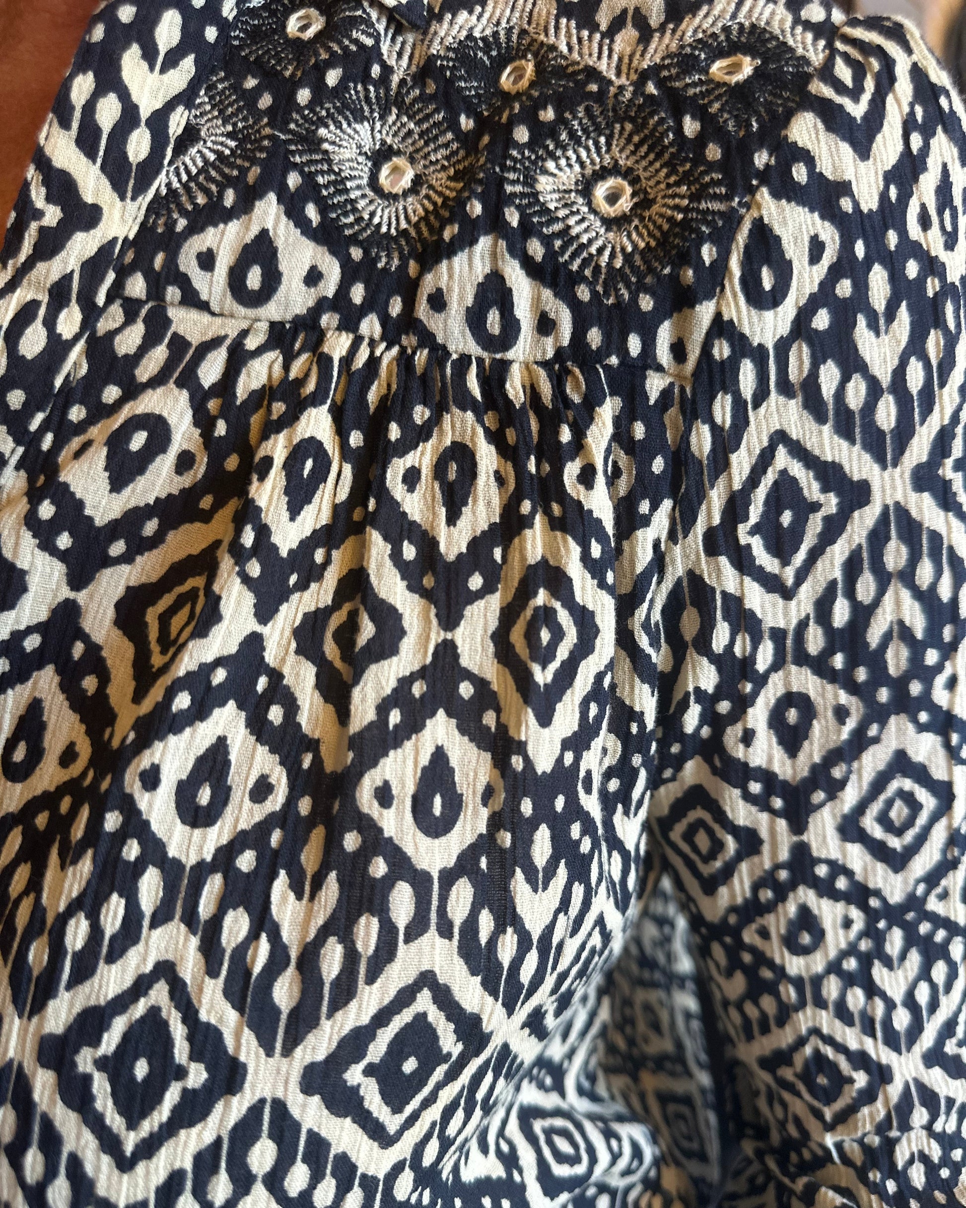 A close-up of the Maison Hotel Ruby Tuesday Ikat Top by Maison Hotel, featuring navy blue and white geometric and diamond-shaped patterns, gathered seams, and textured fabric.