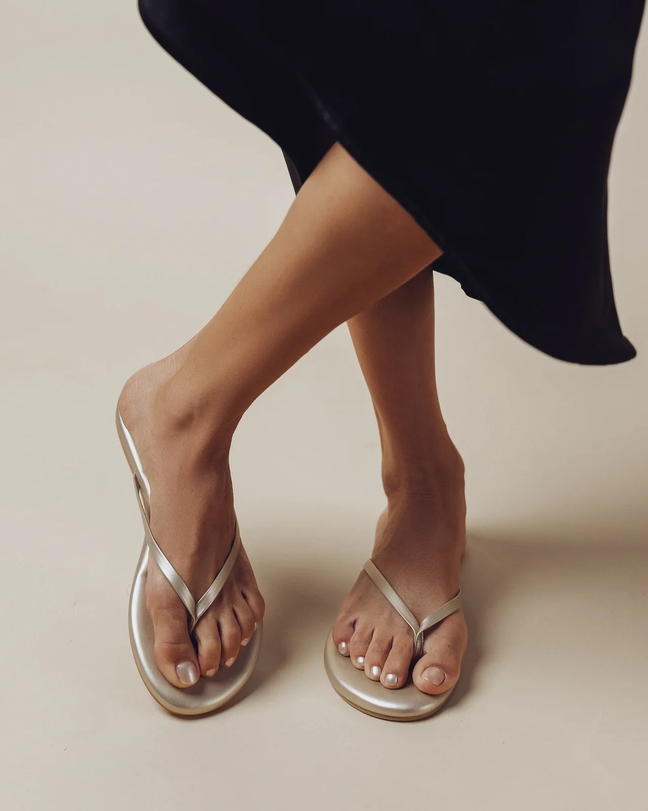 Silver flip-flops worn with a black skirt on a neutral background