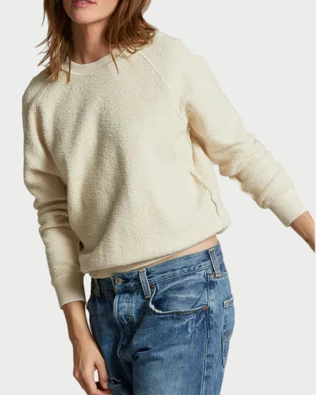 Woman wearing a cream sweater and blue jeans against a plain background