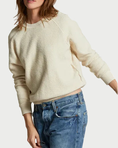 Woman wearing a cream sweater and blue jeans against a plain background
