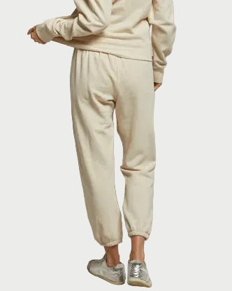 Model wears a cream Perfectwhitetee Johnny Sweatpant in Sugar and matching French terry cotton sweatshirt, seen from the back with silver sneakers against a plain white background.