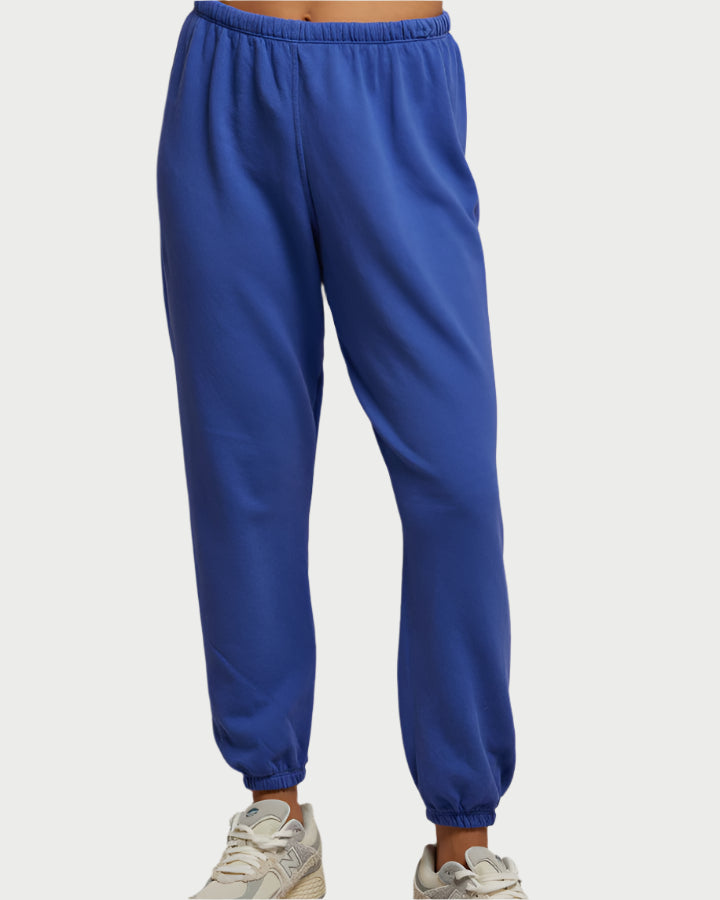 A person wearing Johnny Sweatpants in Violet Blue from perfectwhitetee and beige sneakers, highlighted by the soft feel of French terry cotton. The focus is solely on the lower half against a plain backdrop.