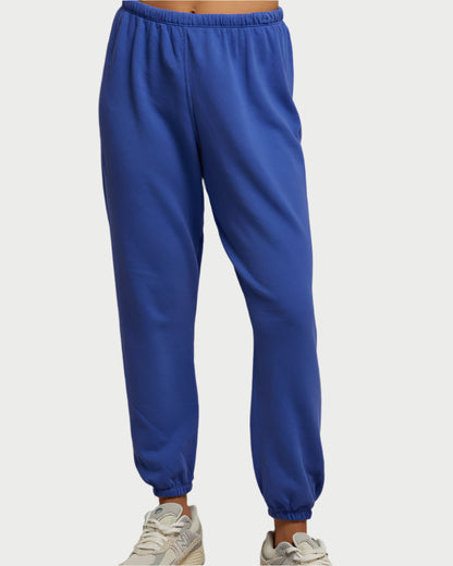A person wearing Johnny Sweatpants in Violet Blue from perfectwhitetee and beige sneakers, highlighted by the soft feel of French terry cotton. The focus is solely on the lower half against a plain backdrop.