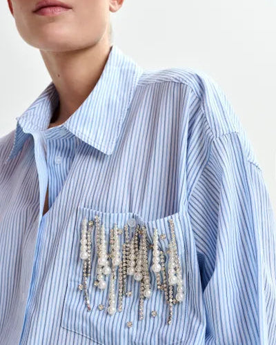 Blue striped shirt with decorative brooches on a plain background