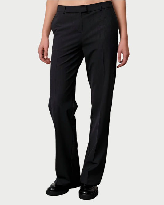 A person models tailored black Herskind Jack Pants wool-blend trousers with black shoes against a plain light background. The straight-leg fit and pressed creases highlight classic menswear tailoring. The upper body is not shown.