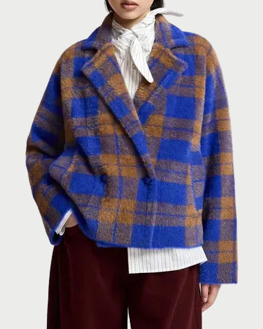 A person wearing the Essentiel Antwerp Karreau Check Cardigan Jacket in blue and brown plaid, paired with a white pinstripe shirt featuring a neck bow and burgundy pants, stands against a light background.