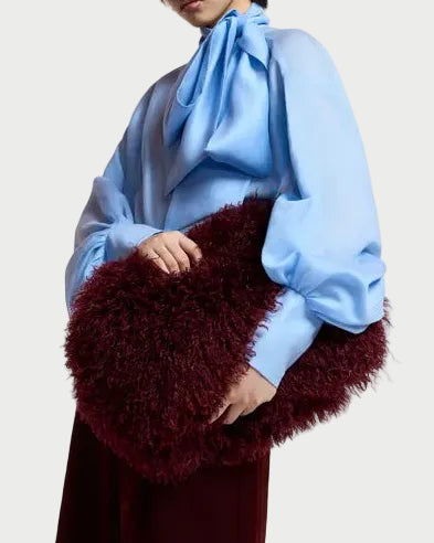 A person in a light blue blouse holds a large, deep red Essentiel Antwerp Katerin Faux Fur Bag.