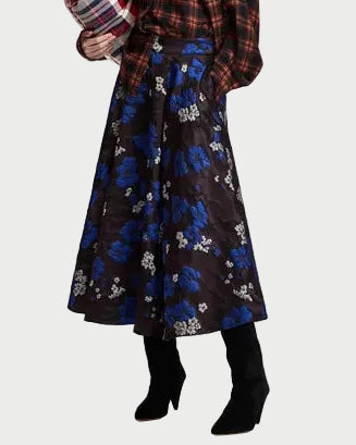 Person wearing the Essentiel Antwerp Kathyanne Circle Midi Skirt by Essentiel Antwerp—a dark floral jacquard midi skirt with blue and white flowers—paired with a plaid shirt and black knee-high boots. The upper part of the person is partially out of the frame.