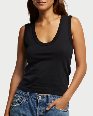 A person wearing the Khara Scoop Tank Black by perfectwhitetee and blue jeans stands with one hand in the pocket against a neutral background, effortlessly blending comfort and style.