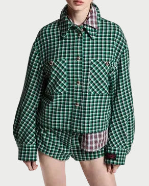 A model wearing a green and black checkered oversized button-up shirt with matching shorts, styled with a plaid shirt peeking out from under the collar and black ankle boots, on a light gray studio background.