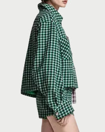 A model is shown from a side-back angle wearing a green and black checkered oversized shirt and matching shorts, paired with black pointed-toe ankle boots, against a plain light gray studio background.