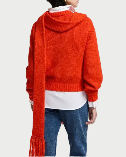 A model shown from the back wearing a bright orange-red knit hooded sweater with a long matching scarf, layered over a white collared shirt and blue jeans, against a plain white studio background.