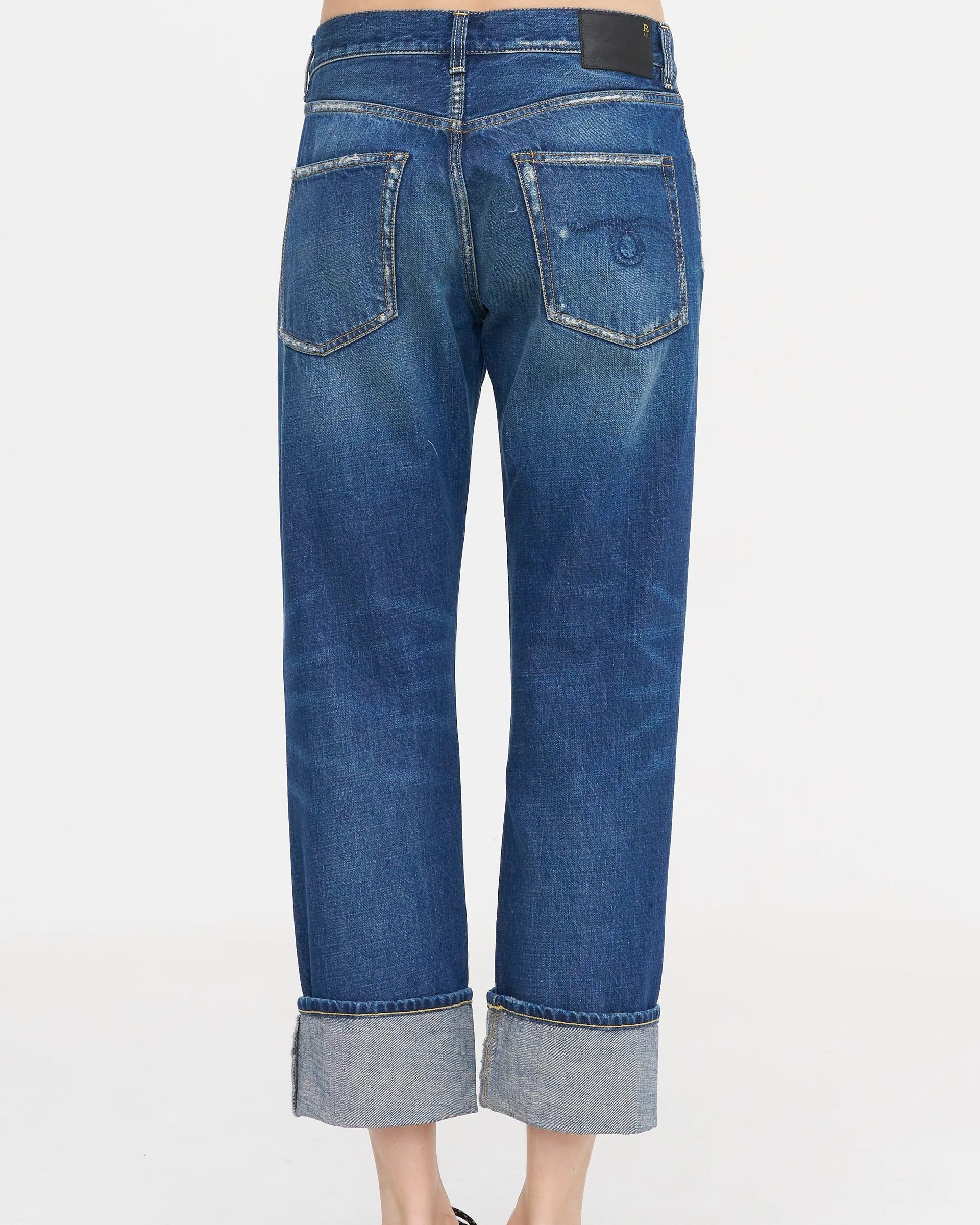 A person is seen from the back wearing the R13 Cuffed Romeo Jean in Oasis Blue, featuring a slim boyfriend fit, Italian denim, cuffed hems above the ankles, two faded back pockets, and a black patch on the cropped waistband.