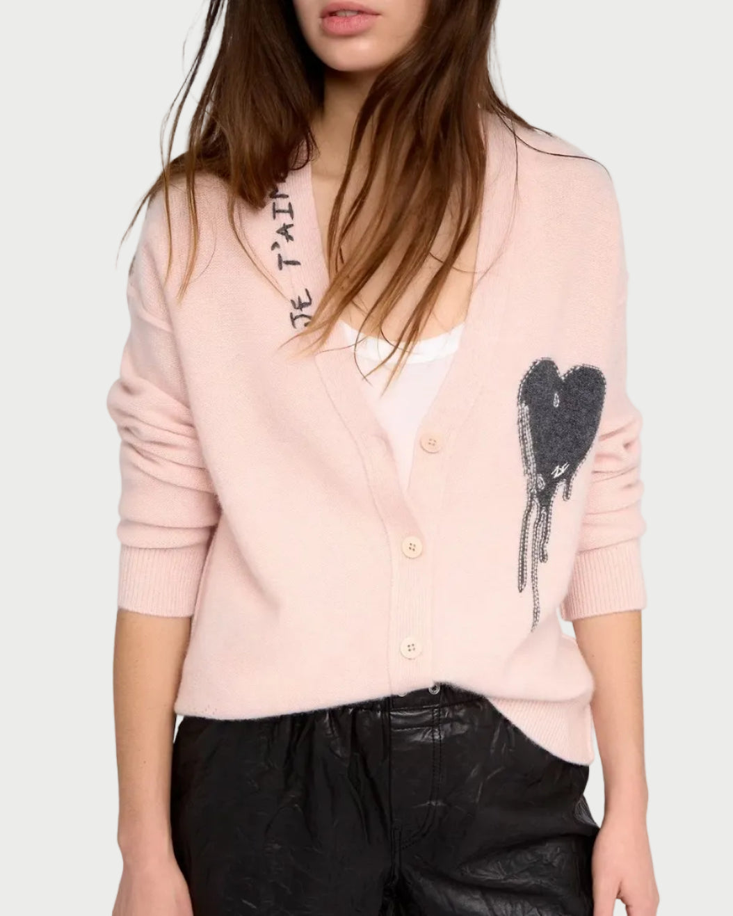 Woman wearing a light pink cardigan with black heart design and black shorts on a white background