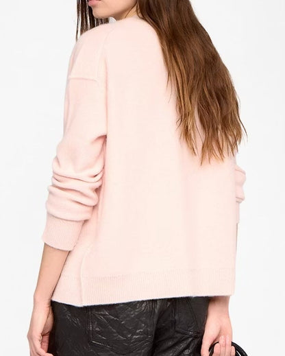 Woman wearing a light pink sweater, black leather shorts, and black boots on a white background