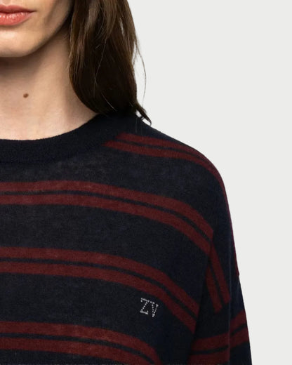 Close-up of a woman wearing a dark navy and burgundy striped knit sweater with a small white embroidered 'ZV' logo on the chest, against a light gray background.