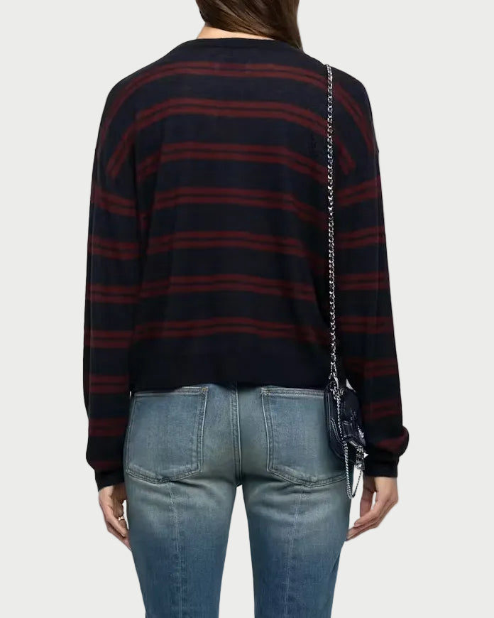 A woman shown from the back wearing a navy and red striped long-sleeve knit top, blue jeans, and carrying a small dark shoulder bag against a light gray studio background.