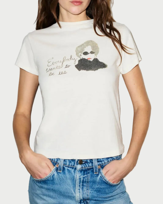 Woman wearing a white t-shirt with a graphic design and sunglasses, standing against a plain background
