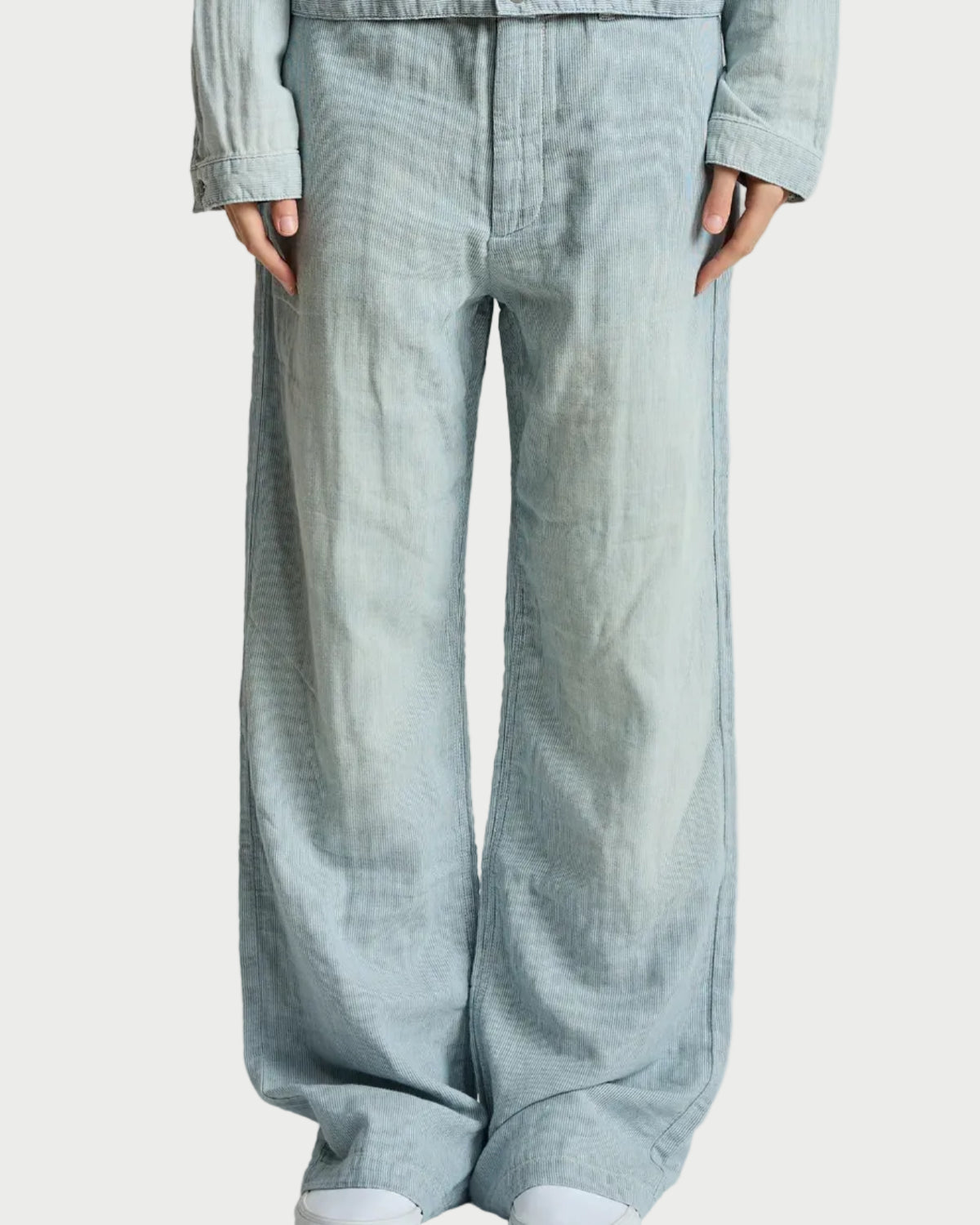 A person wearing light blue wide-leg denim pants with a matching light blue cropped jacket and white sneakers, shown from the chest down against a plain light gray studio background.
