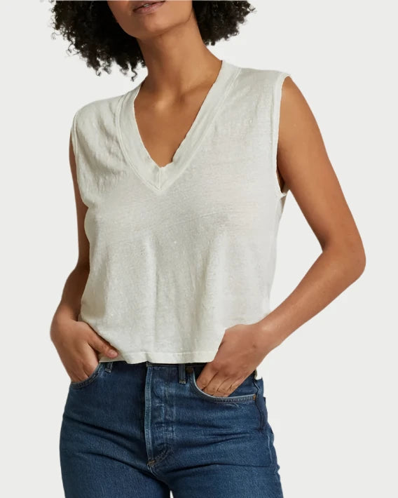 A person with short, curly hair is wearing the Lucy V neck Tank from perfectwhitetee, paired with blue jeans. They have their hands in their jeans pockets and are standing against a plain, light-colored background.