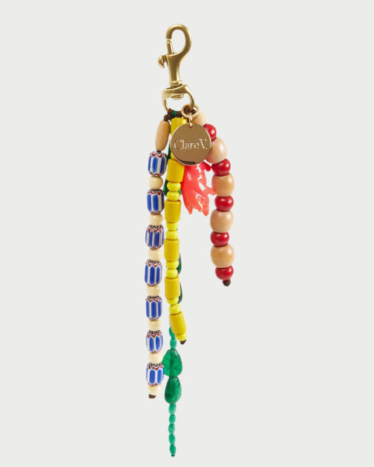 The CLARE V. Le Long Beaded Tassel keychain features vibrant blue, yellow, green, red, and natural wood beads with a gold clasp and engraved round tag—a striking bag charm for any accessory lover.