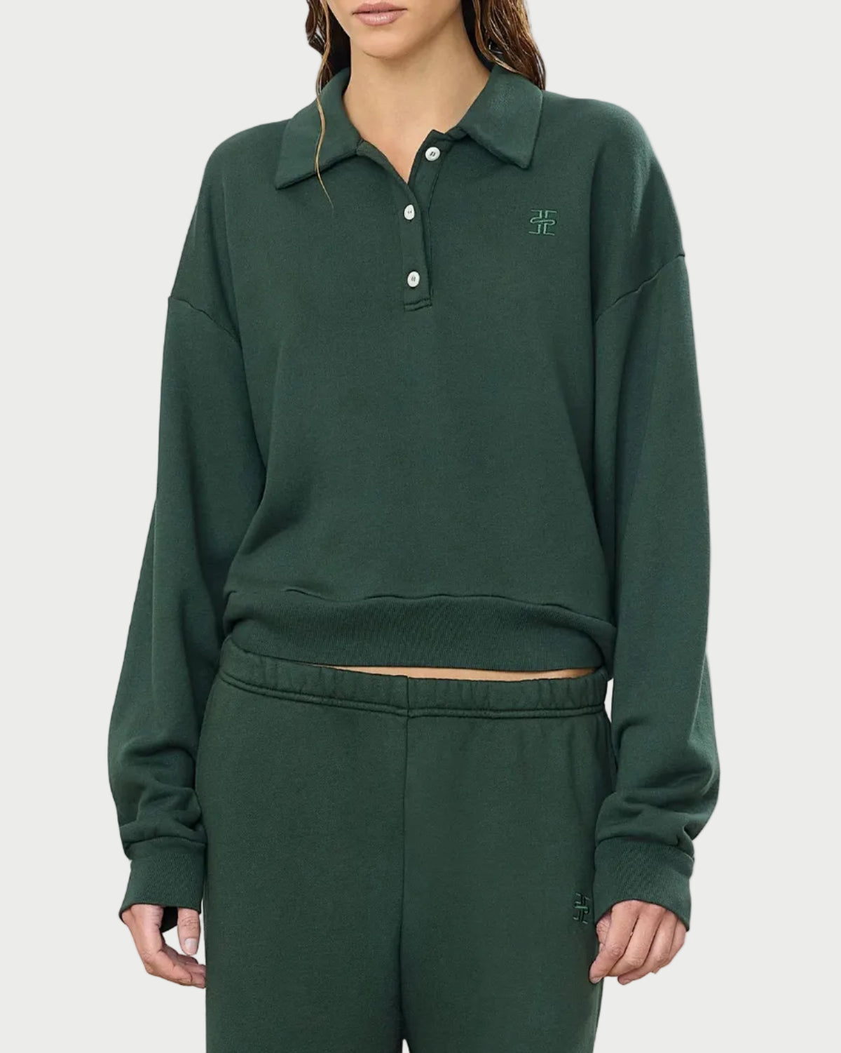 A person dressed in the Éterne Cropped Polo Sweatshirt by Eterne—a dark green, relaxed-fit lounge set featuring a collared pullover made from soft French terry fabric with buttons and a small embroidered logo on the chest—stands against a plain white background.