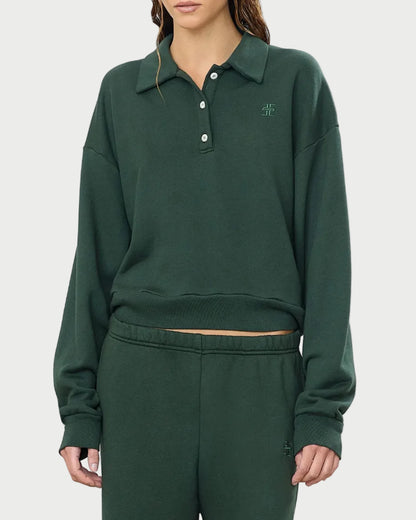 A person dressed in the Éterne Cropped Polo Sweatshirt by Eterne—a dark green, relaxed-fit lounge set featuring a collared pullover made from soft French terry fabric with buttons and a small embroidered logo on the chest—stands against a plain white background.