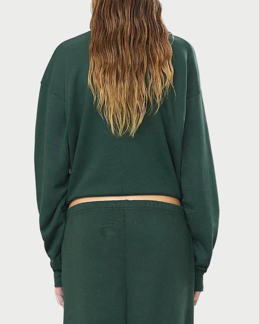 A person with long, wavy, light brown hair is shown from the back against a white background wearing the Éterne Cropped Polo Sweatshirt and matching pants by Eterne in a relaxed fit. The dark green outfit is crafted from soft French terry for added comfort.
