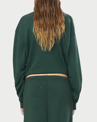 A person with long, wavy, light brown hair is shown from the back against a white background wearing the Éterne Cropped Polo Sweatshirt and matching pants by Eterne in a relaxed fit. The dark green outfit is crafted from soft French terry for added comfort.