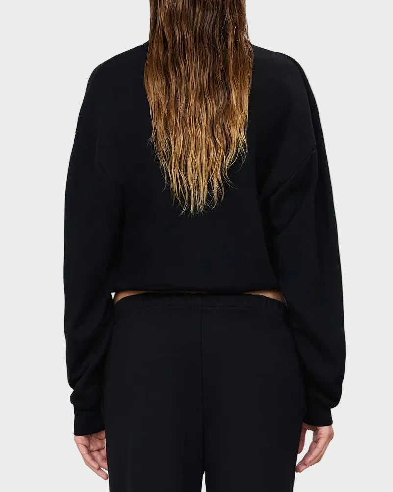 A person with long, wet, wavy brown hair is shown from the back, wearing the Éterne Cropped Polo Sweatshirt by Eterne in black and matching black pants, standing against a plain light background.