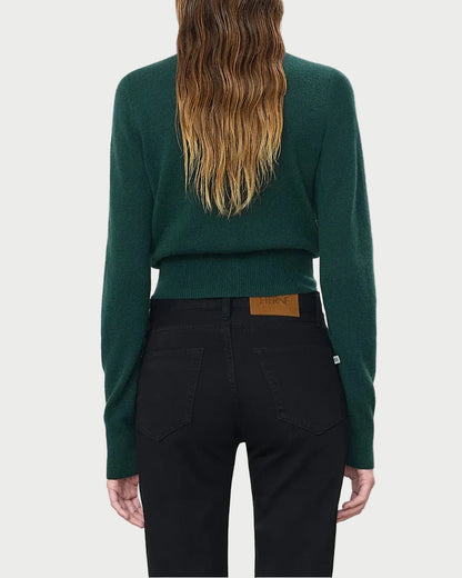 A person with long, wavy brown hair is shown from behind against a plain light background, wearing the Eterne Éterne Reese Cashmere Sweater in dark green slim fit paired with black jeans.