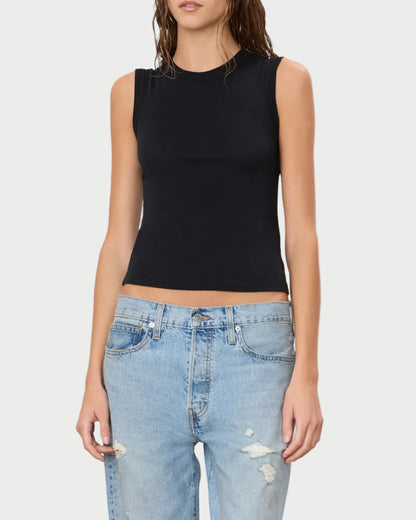 A woman wearing the Éterne Fitted Muscle Tank by Eterne—a sleeveless black top crafted from a soft cotton-modal blend—and light blue ripped jeans stands against a plain white background.