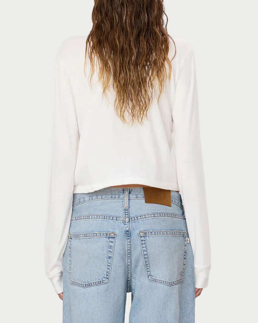 A person with long wavy hair is shown from the back against a plain light background, wearing the Eterne Long Sleeve Boxy Tee—crafted from a soft cotton-modal blend in crisp white—with light blue high-waisted jeans. The relaxed, boxy fit of this Éterne tee adds effortless comfort to the look.