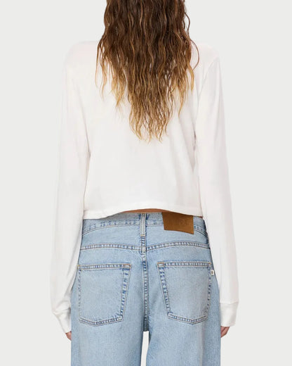 A person with long wavy hair is shown from the back against a plain light background, wearing the Eterne Long Sleeve Boxy Tee—crafted from a soft cotton-modal blend in crisp white—with light blue high-waisted jeans. The relaxed, boxy fit of this Éterne tee adds effortless comfort to the look.