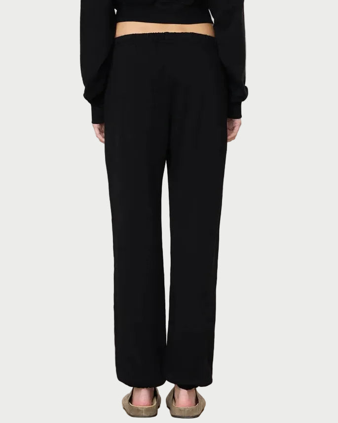 A person stands facing away against a light gray background, wearing Éterne Boyfriend Pocket Sweatpants by Eterne in black, paired with a black top and brown sandals.
