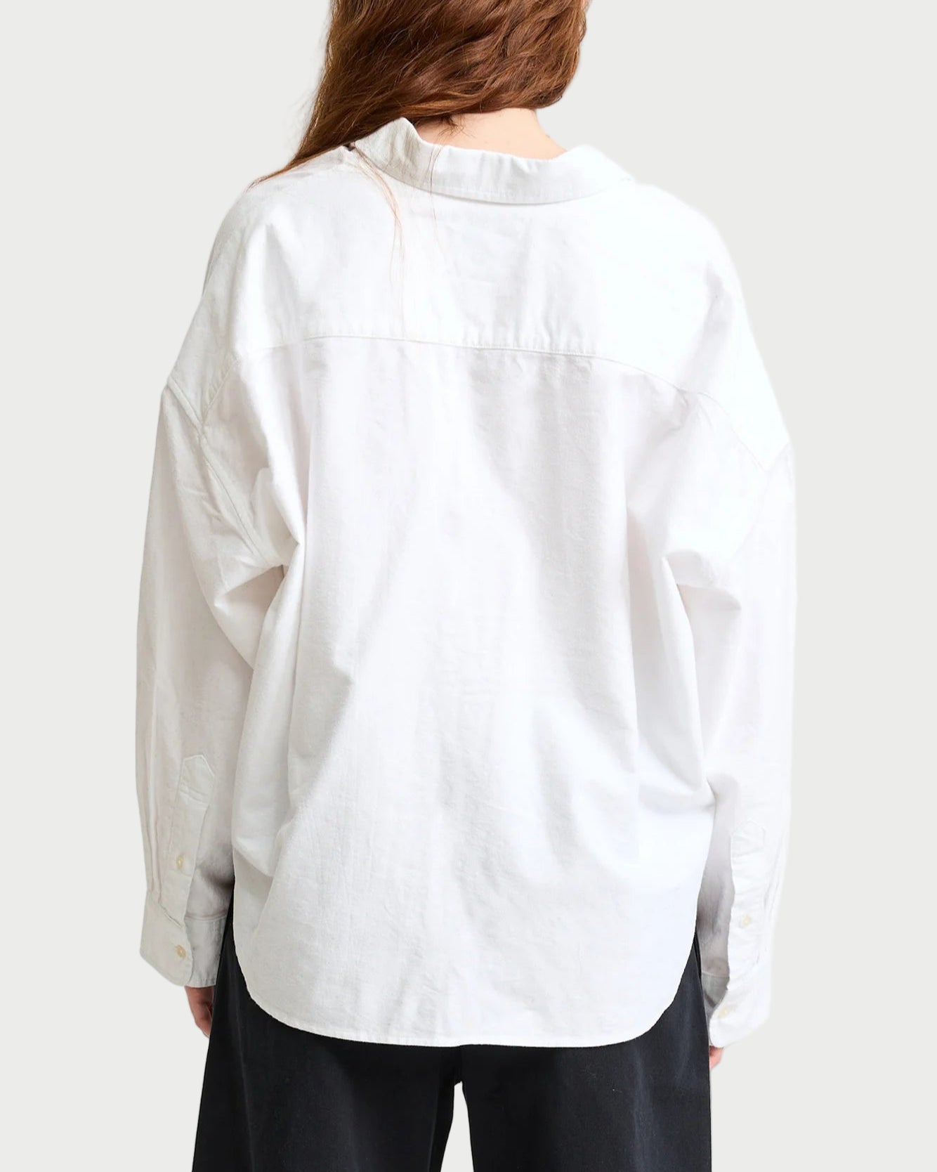 A person with long brown hair, seen from behind, wears a loose-fitting Denimist Cropped Button Front Shirt and black pants against a plain background.