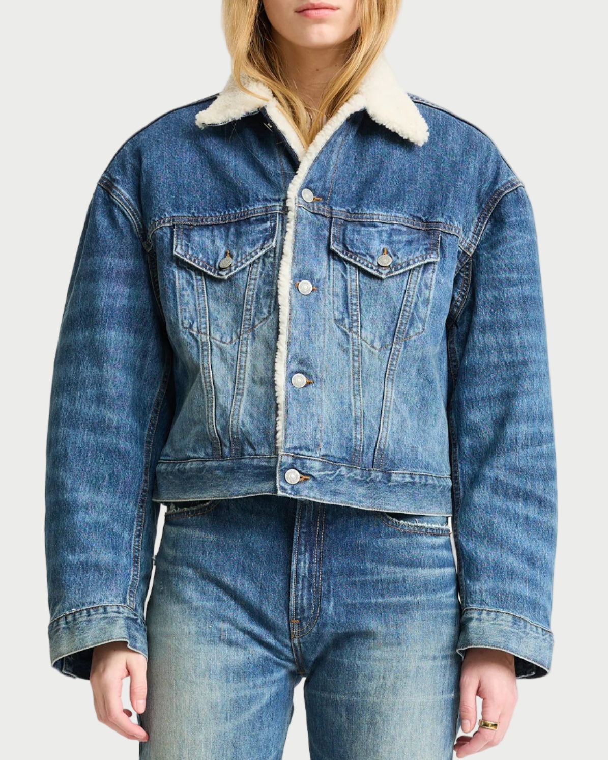 Person wearing a denim jacket with white fur lining on a plain background