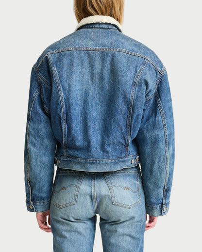 Person wearing a blue denim jacket and jeans on a white background