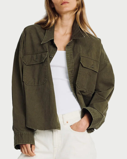 Woman wearing an olive green jacket over a white top and pants on a light gray background