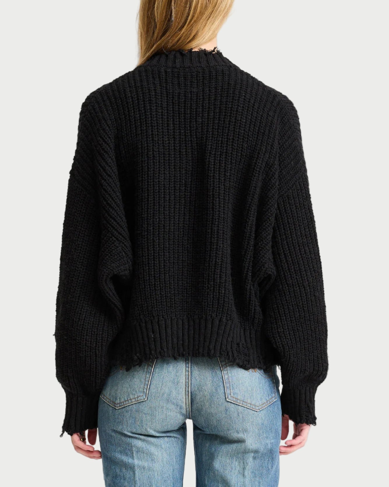 Person wearing a black sweater and blue jeans on a white background