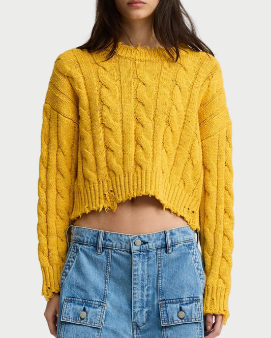 Woman wearing a yellow cable knit sweater and denim shorts on a white background