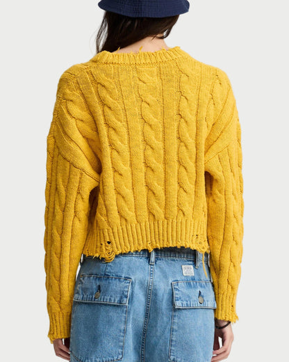 Person wearing a yellow cable knit sweater and blue denim shorts with a navy bucket hat on a white background