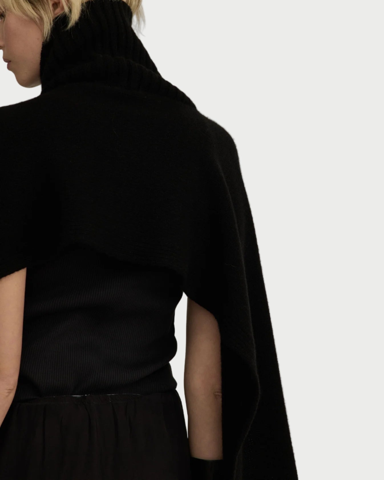 Person wearing a black turtleneck and cape against a plain background