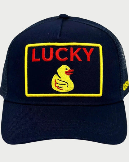 The Soulbyrd Lucky Duck Trucker Hat is navy blue with an adjustable snapback and features a yellow-bordered embroidered "LUCKY" patch in red above a yellow duck, centered on the front.