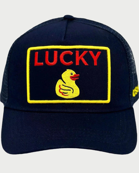 The Soulbyrd Lucky Duck Trucker Hat is navy blue with an adjustable snapback and features a yellow-bordered embroidered "LUCKY" patch in red above a yellow duck, centered on the front.
