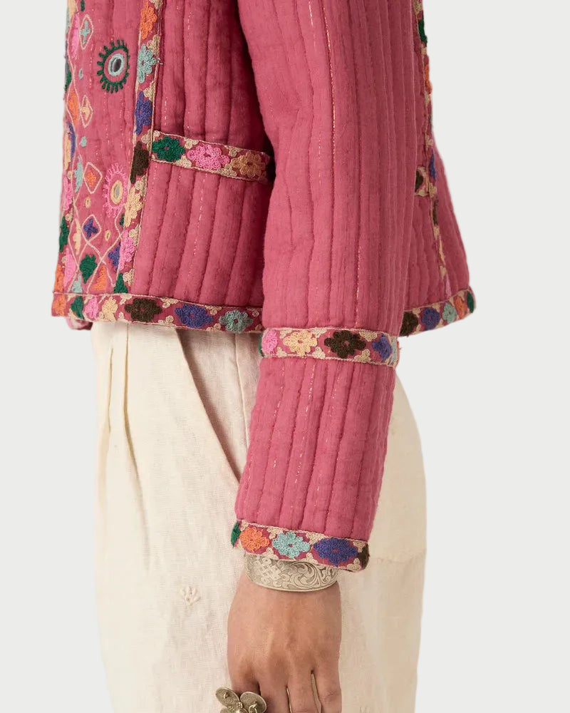 Close-up of a pink embroidered traditional outfit with white pants on a plain background