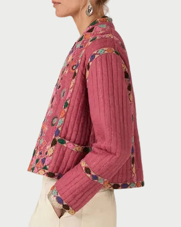 Woman wearing a pink pleated blouse with floral patterns and beige pants on a white background